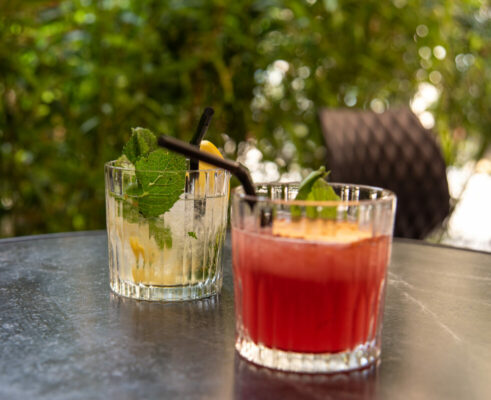 Deux cocktails de Saint-Valentin servis côte à côte, décorés de fruits frais, dans une ambiance de bar chaleureuse et intimiste, idéale pour un verre en amoureux.