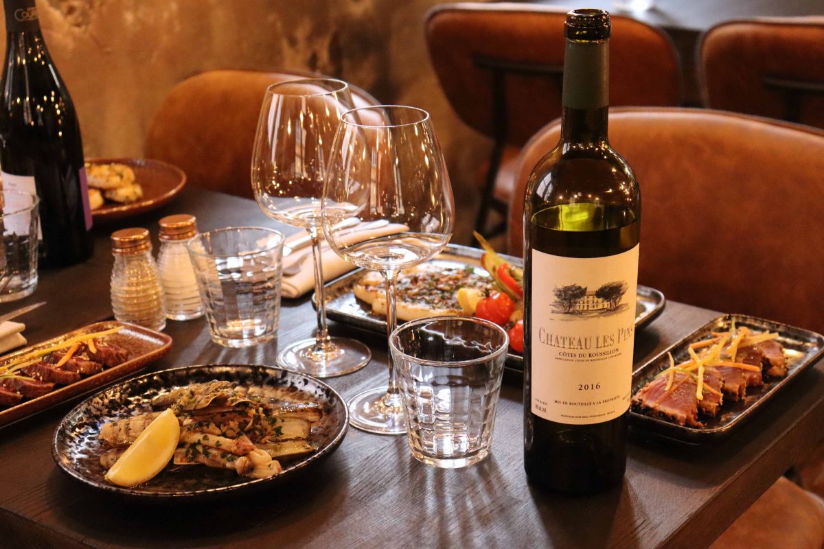 table de restaurant avec des plats cuits à la plancha et une bouteille de vin rouge